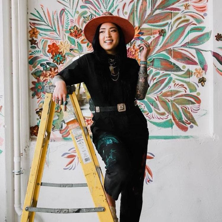 A girl standing on a ladder in front of a floral mural